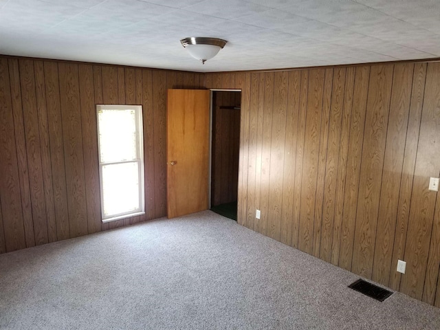 unfurnished room featuring carpet, visible vents, and wooden walls