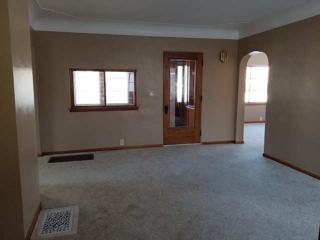 carpeted empty room featuring visible vents, baseboards, and arched walkways