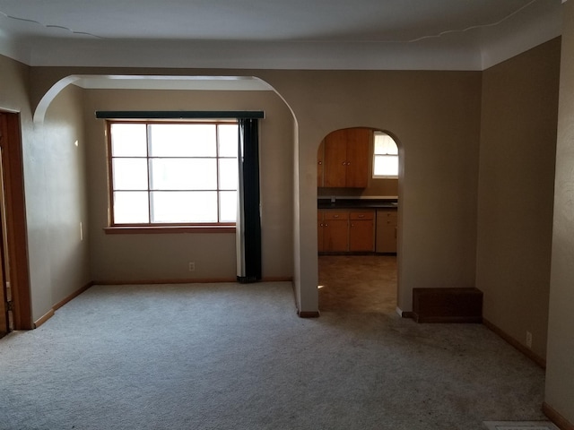 empty room with baseboards, arched walkways, and light carpet