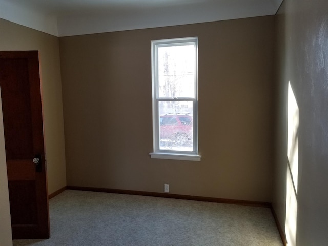 spare room featuring light carpet, baseboards, and a wealth of natural light