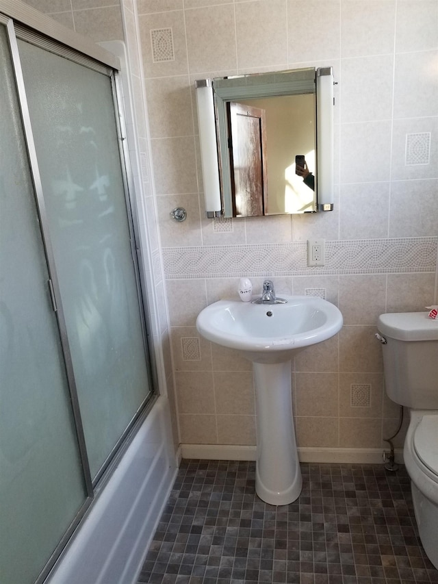 bathroom featuring toilet, enclosed tub / shower combo, and tile walls