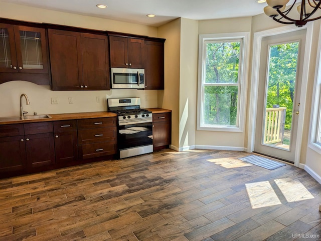 kitchen featuring dark brown cabinetry, sink, hanging light fixtures, dark hardwood / wood-style flooring, and stainless steel appliances