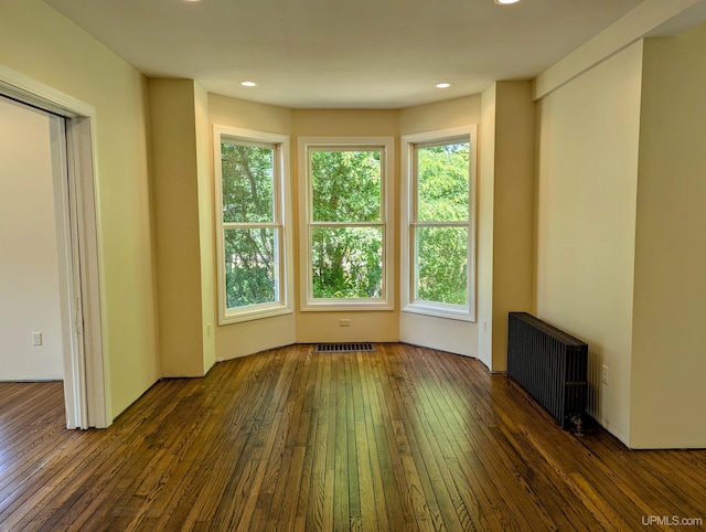 empty room featuring radiator heating unit, dark hardwood / wood-style floors, and a healthy amount of sunlight