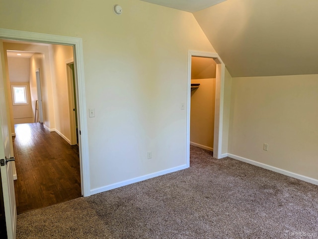 unfurnished bedroom featuring carpet, a closet, vaulted ceiling, and a walk in closet