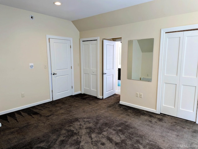 unfurnished bedroom featuring multiple closets, vaulted ceiling, and dark colored carpet