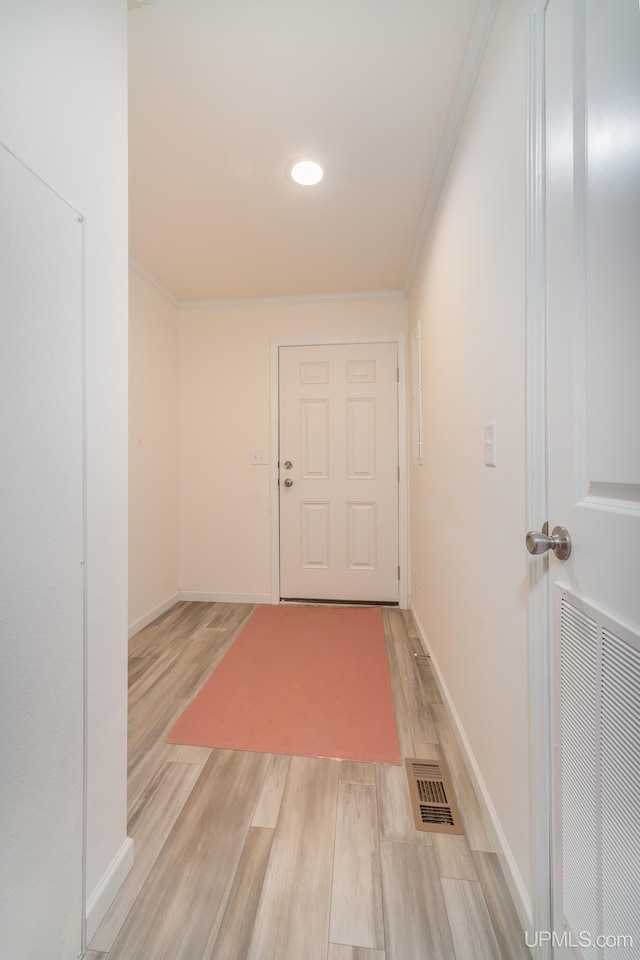 hallway with light wood-type flooring, visible vents, baseboards, and crown molding