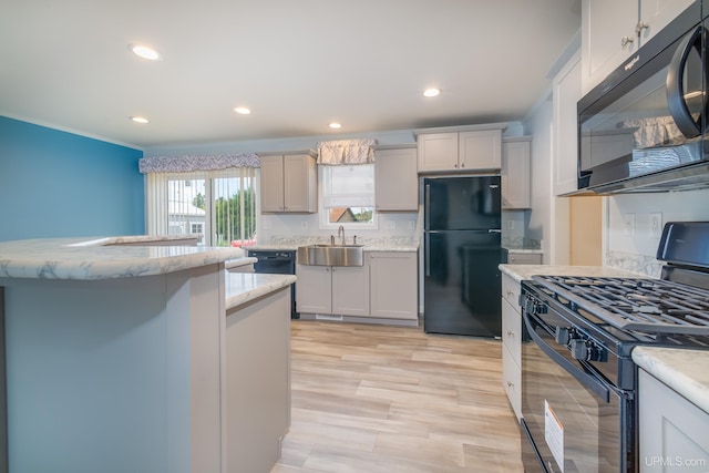 kitchen with a sink, light stone counters, black appliances, and recessed lighting