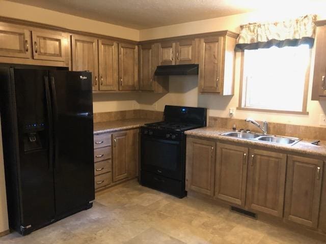 kitchen featuring under cabinet range hood, brown cabinetry, visible vents, a sink, and black appliances