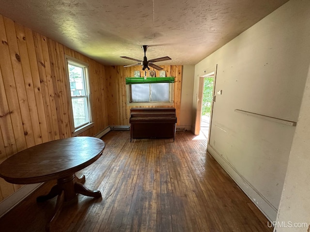 unfurnished dining area with ceiling fan, dark wood-type flooring, a textured ceiling, and wooden walls