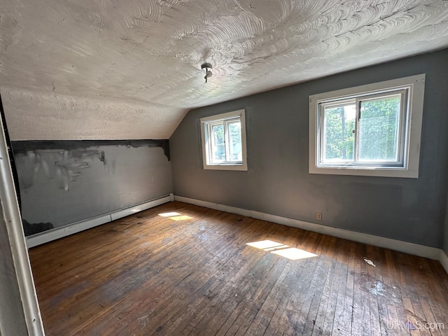 additional living space with a baseboard heating unit, a wealth of natural light, lofted ceiling, and hardwood / wood-style floors