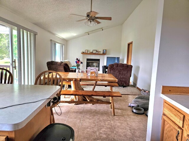 dining area featuring high vaulted ceiling, a textured ceiling, a tile fireplace, light tile patterned flooring, and ceiling fan