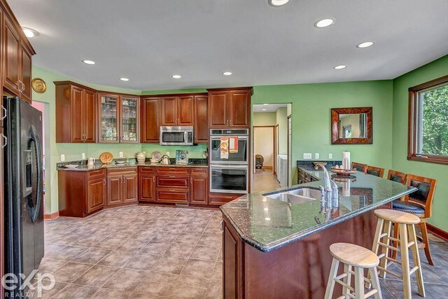 kitchen with stainless steel appliances, a breakfast bar area, sink, light tile patterned flooring, and dark stone counters