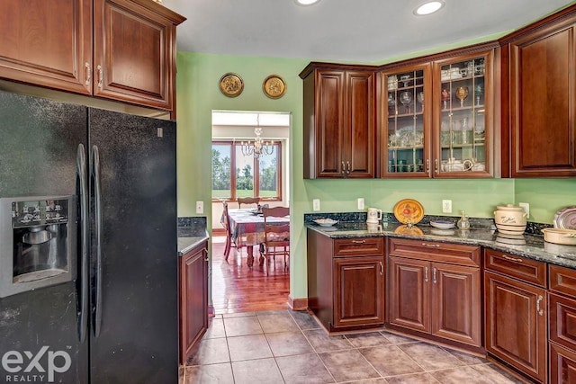 kitchen with an inviting chandelier, black fridge with ice dispenser, dark stone counters, and light tile patterned flooring