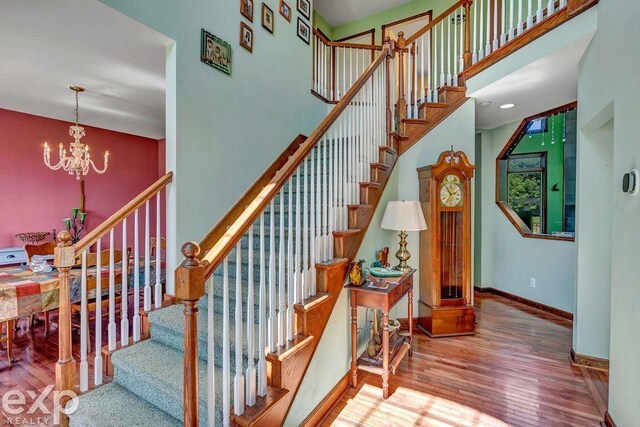 stairway featuring wood-type flooring, a high ceiling, and an inviting chandelier