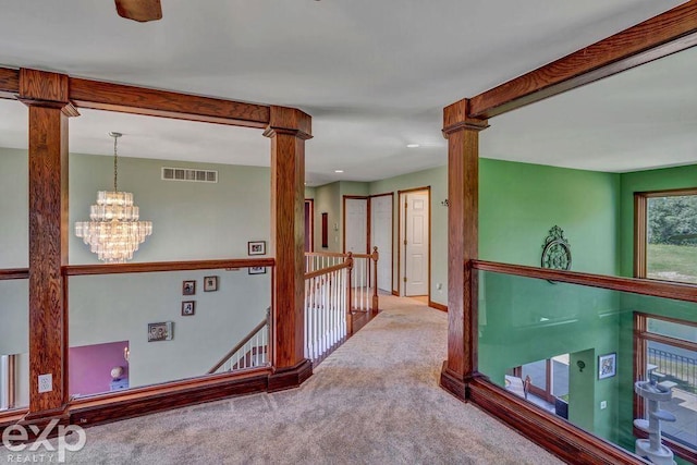 corridor featuring a notable chandelier, beam ceiling, decorative columns, and carpet flooring