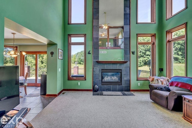 living room featuring a tiled fireplace, carpet, ceiling fan, and a high ceiling