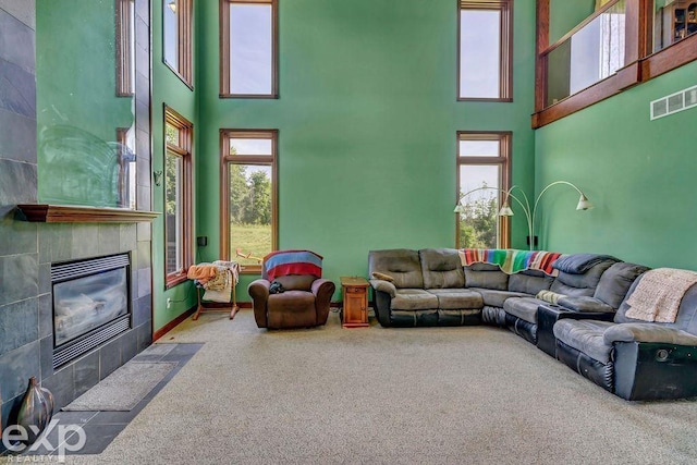 carpeted living room featuring a tiled fireplace, a towering ceiling, and a wealth of natural light