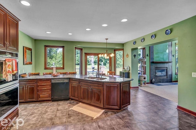 kitchen featuring dark stone counters, dishwasher, light tile patterned floors, a tile fireplace, and sink