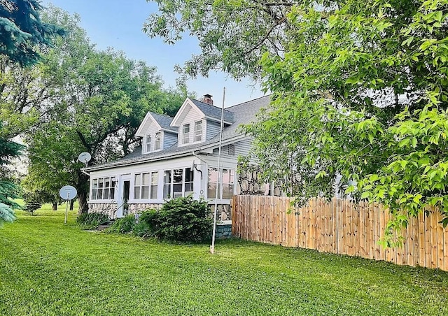 view of front of house with a sunroom, a chimney, fence, and a front yard