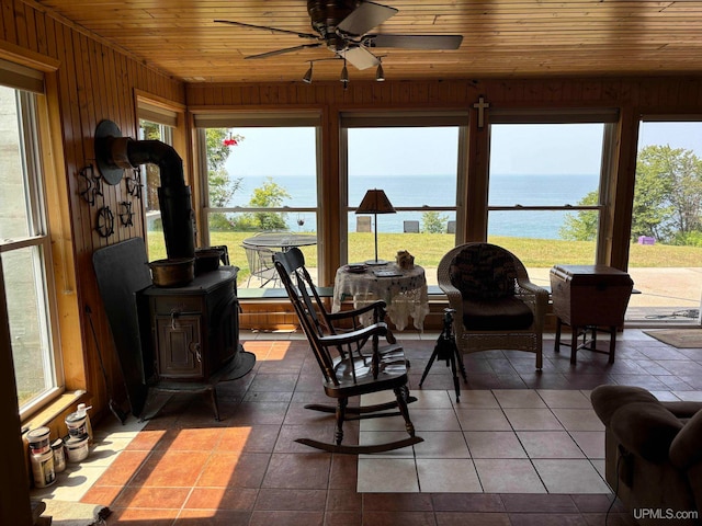 sunroom / solarium featuring wooden ceiling, a wood stove, ceiling fan, and a water view