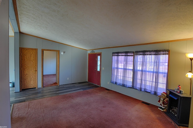 unfurnished living room with dark carpet, vaulted ceiling, crown molding, and a textured ceiling