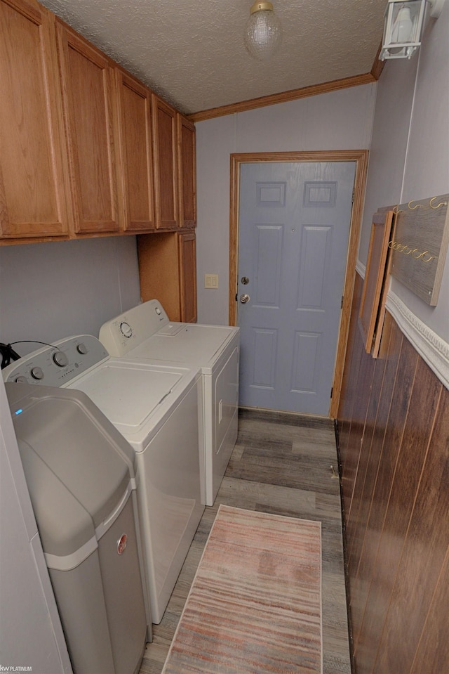 clothes washing area with light wood-type flooring, cabinets, washing machine and clothes dryer, a textured ceiling, and crown molding