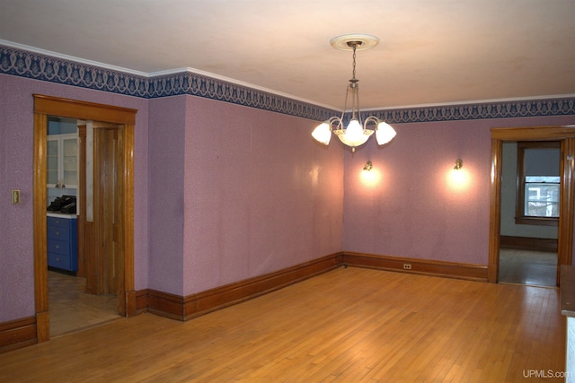 spare room with ornamental molding, baseboards, light wood-type flooring, and a chandelier