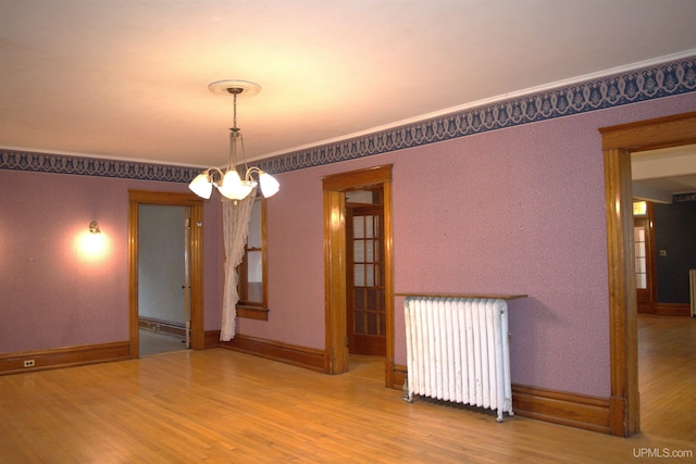 spare room with radiator heating unit, a notable chandelier, wood finished floors, and baseboards