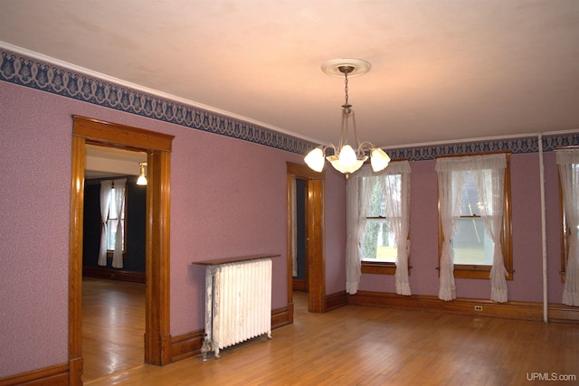 empty room featuring baseboards, an inviting chandelier, ornamental molding, radiator heating unit, and wood-type flooring