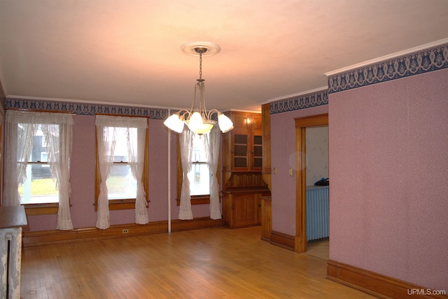 unfurnished dining area with a chandelier, light wood-style floors, baseboards, and ornamental molding