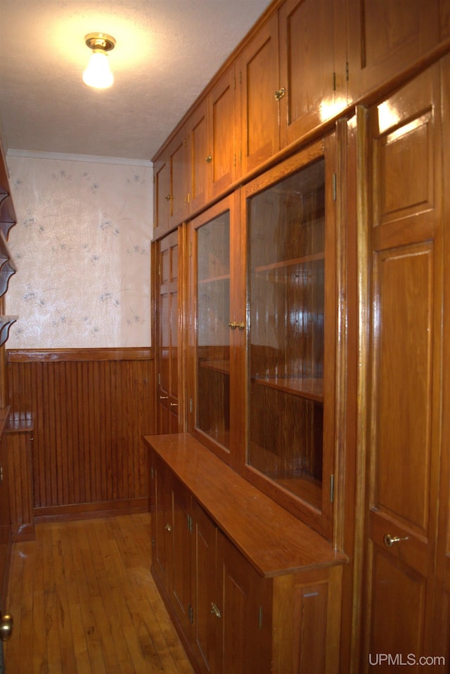 hall with light wood finished floors, wainscoting, and wooden walls