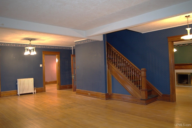 unfurnished living room featuring radiator heating unit, stairs, wallpapered walls, and wood finished floors