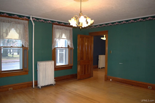 empty room with ornamental molding, radiator, an inviting chandelier, and wood finished floors