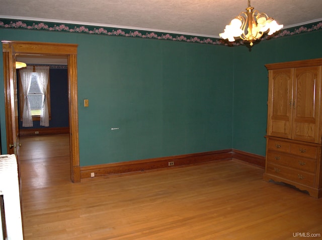 spare room featuring crown molding, baseboards, light wood-type flooring, and a notable chandelier