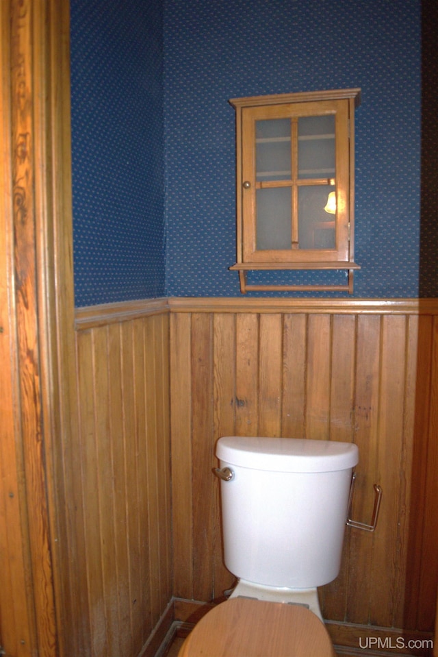 bathroom featuring wooden walls, wainscoting, wallpapered walls, and toilet