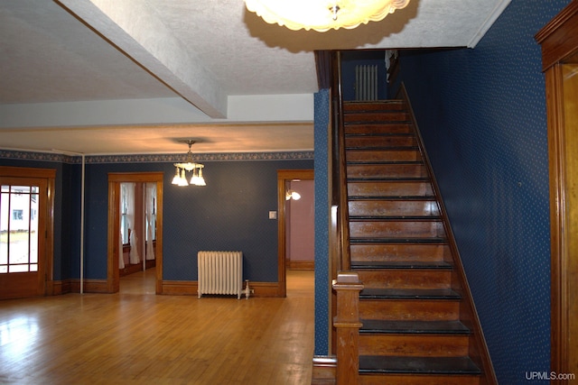 stairs with radiator heating unit, wood finished floors, wallpapered walls, baseboards, and beam ceiling