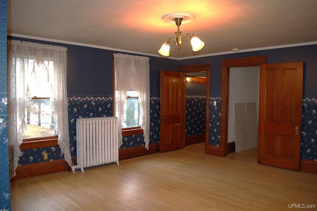 spare room featuring a chandelier, wallpapered walls, radiator, and crown molding