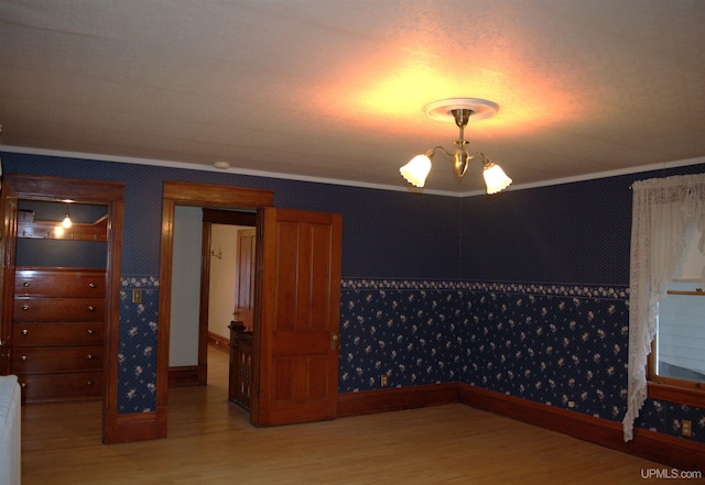 unfurnished room featuring baseboards, light wood-type flooring, a chandelier, crown molding, and wallpapered walls