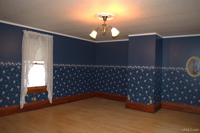 unfurnished room with a notable chandelier, wallpapered walls, crown molding, and wood finished floors