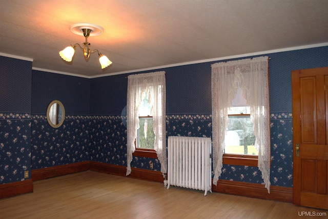 spare room featuring radiator, an inviting chandelier, wood finished floors, and wallpapered walls