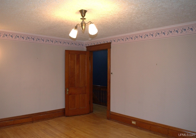 unfurnished room featuring light wood-style floors, baseboards, ornamental molding, and a textured ceiling