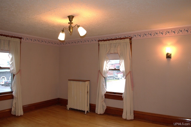 spare room with light wood-style floors, a textured ceiling, radiator heating unit, ornamental molding, and baseboards
