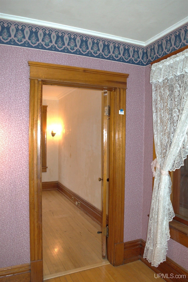 corridor featuring baseboards, wallpapered walls, ornamental molding, and wood finished floors