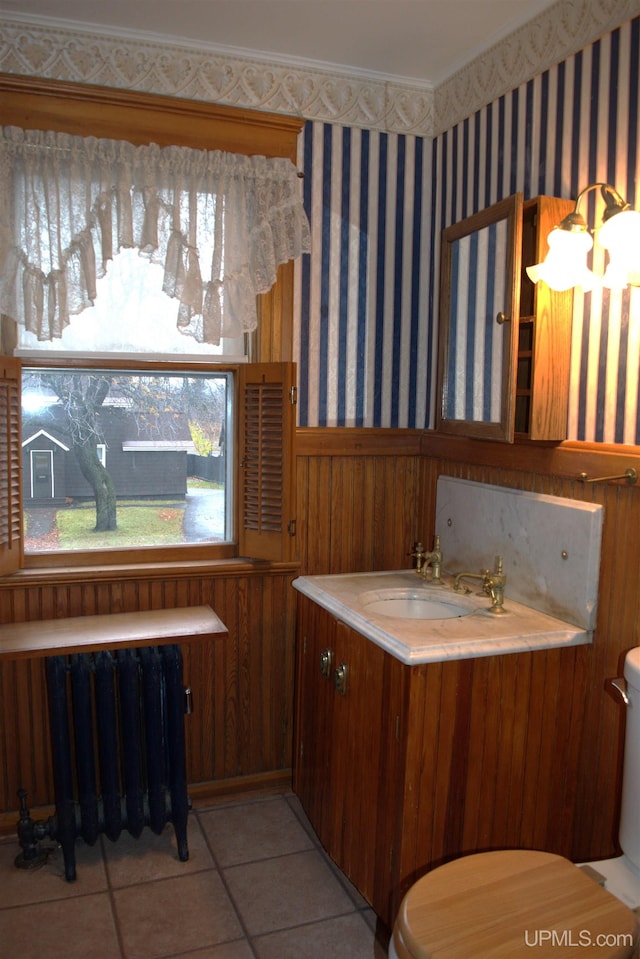 half bathroom with radiator, tile patterned flooring, a wainscoted wall, toilet, and wallpapered walls