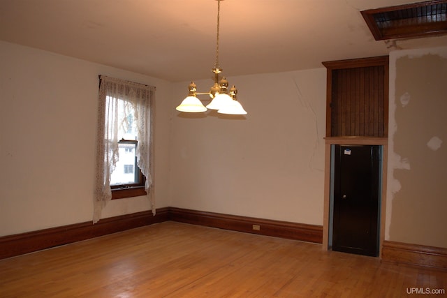 empty room with light wood-type flooring, an inviting chandelier, and baseboards