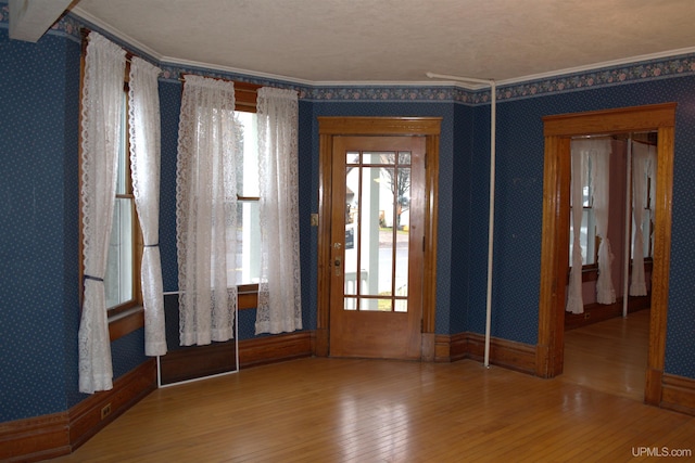 foyer with a wealth of natural light, wallpapered walls, hardwood / wood-style floors, and crown molding