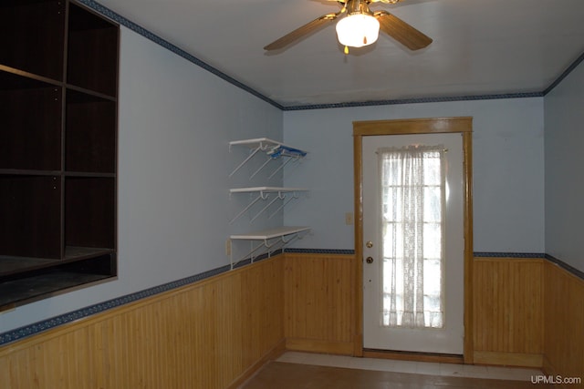 doorway to outside featuring ornamental molding, wood walls, a wainscoted wall, and ceiling fan
