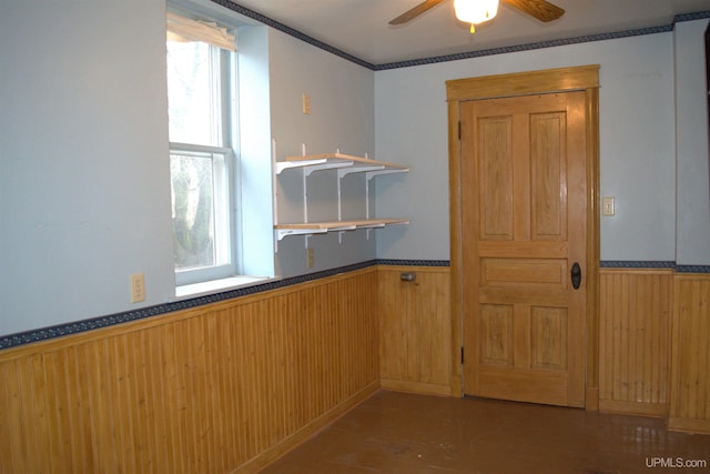 unfurnished dining area featuring wooden walls, a wealth of natural light, ceiling fan, and wainscoting