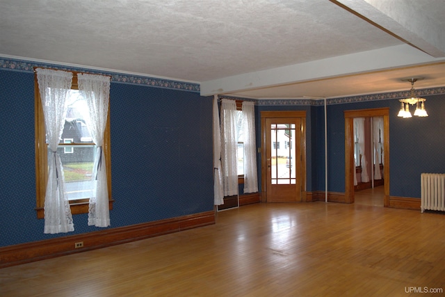 empty room featuring a textured ceiling, radiator, baseboards, and wallpapered walls