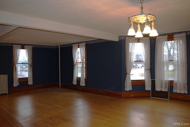 empty room featuring beam ceiling, radiator heating unit, a notable chandelier, and wood finished floors